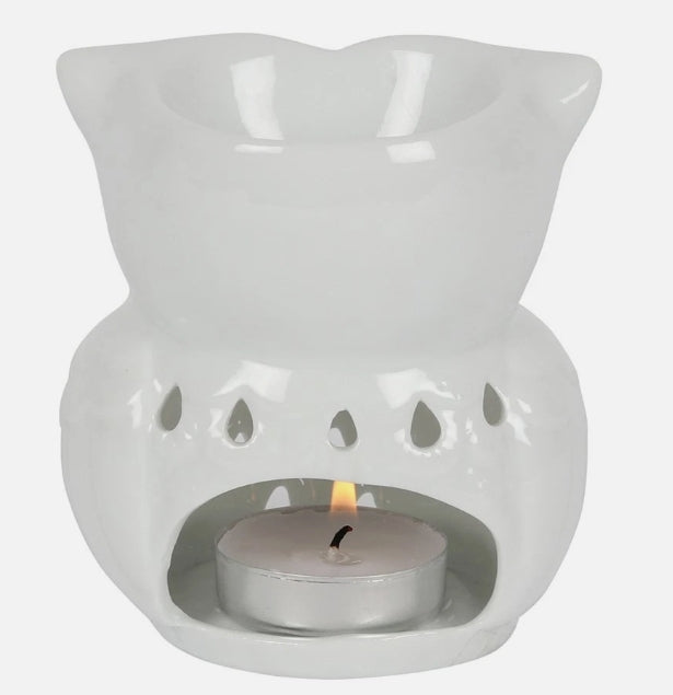 A white ceramic owl tea light wax warmer with a small lit tealight candle inside, shown against a plain light  background.