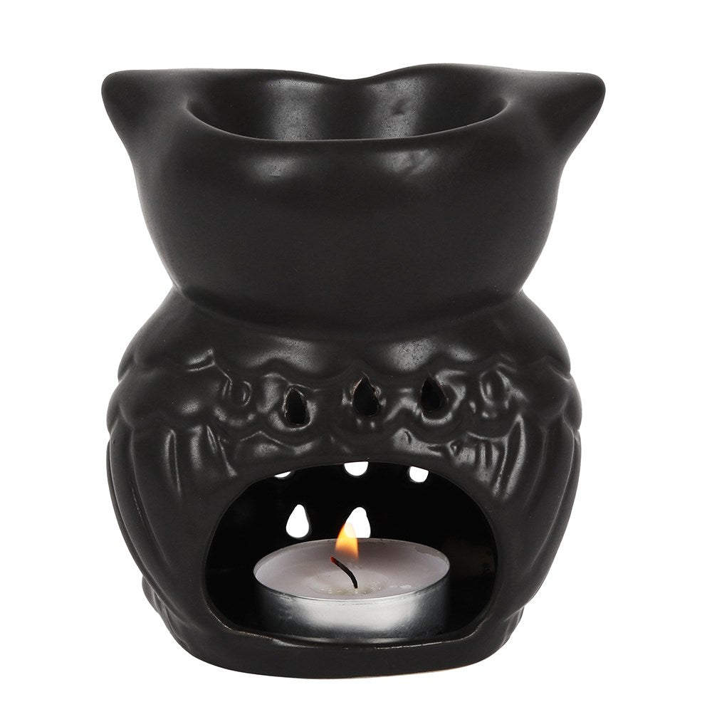 Black ceramic owl-shaped oil burner with a lit tealight candle inside on a white background