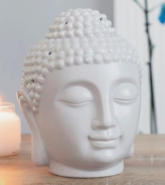 A grey ceramic Buddha head sculpture with closed eyes and a serene expression, styled on a wooden surface next to a lit candle.