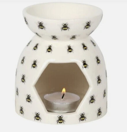 A white ceramic oil burner candle holder decorated with a repeating pattern of black and yellow bumblebees, featuring a hexagonal opening with a lit tealight candle inside.